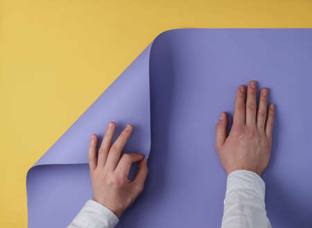 Male hands bend a sheet of colored paper yellow background, copy space. top viewの写真素材