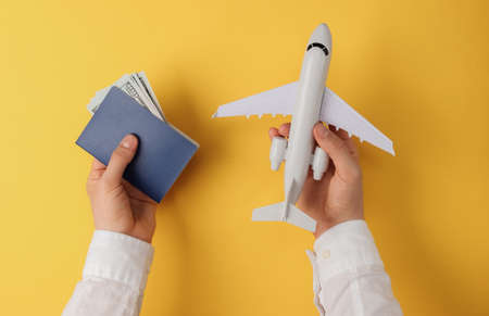 Men's hands hold passport with money plane yellow background. top view