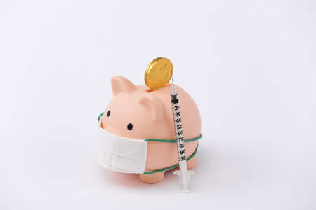 Piggy bank in medical mask with syringe, coin on white background. vaccination. economic disease. financial crisis. Covid-19 pandemicの写真素材