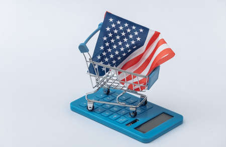 Mini supermarket trolley with USA flag, calculator on white background. american shopping