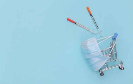 Shopping trolley in medical mask with syringes on blue background. healthcare. top viewの写真素材