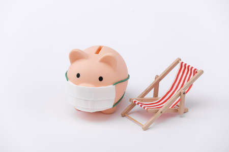 Piggy bank in medical mask and beach chair. white background. Beach holidays during the pandemic...