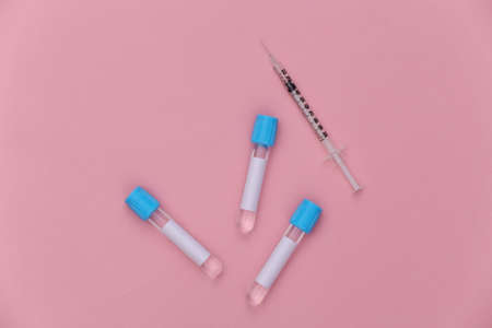 Medical test tubes with syringe on pink pastel background. top view
