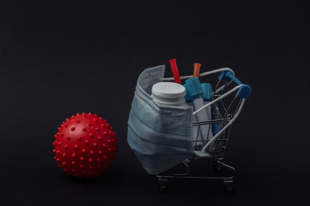 Shopping trolley in medical mask with test tubes, syringes, pills bottle and virus strain model on black background. healthcareの写真素材