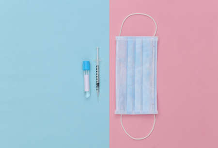 Medical test tube with syringe and face mask on blue pink pastel background. vaccination. top view