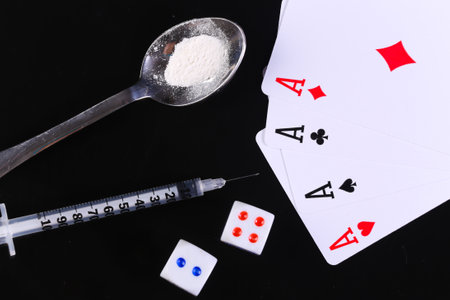 Drug and gambling addiction. Spoon with a drug powder, syringe, dice and four aces isolated on black...