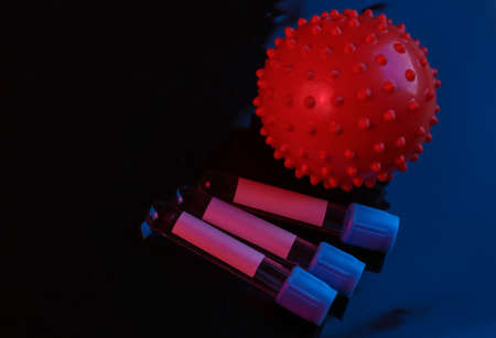 The vaccine is invented! Virus strain model and test tubes on black background with red blue lightの写真素材
