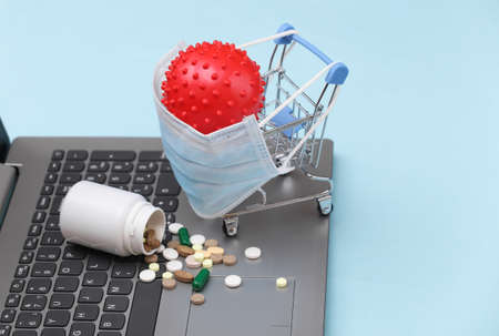 Shopping trolley in medical mask with pills bottle on laptop keyboard. blue background. pandemic....