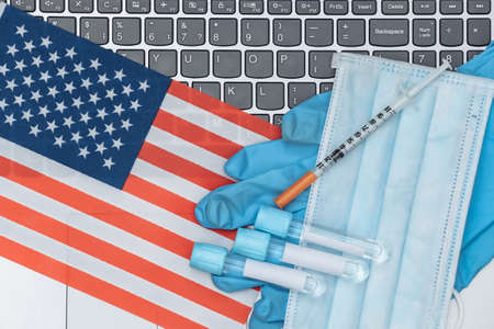Medical test tubes, face mask, gloves with syringe on laptop keyboard with USA flag.