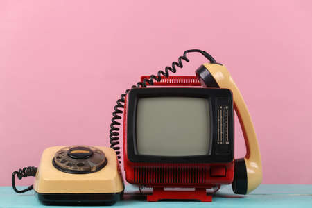 Red retro old portable mini tv set with rotary telephone on pink background.の写真素材