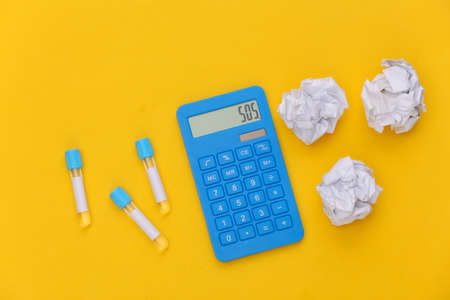 Test tubes, calculator with crumpled paper balls on yellow background. top viewの写真素材