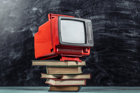 Retro tv and stack of books on blackboard background. TV distance learning.