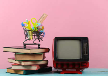 Retro tv and stack of books, shopping trolley with school supplies on pink background. TV distance learning.の写真素材