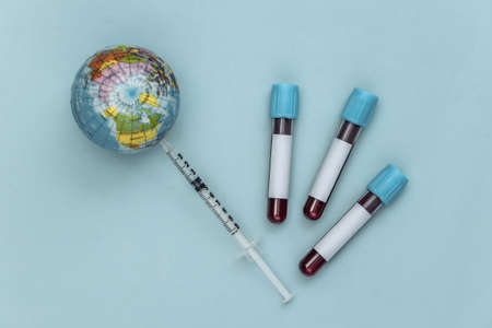 Global blood testing covid-19. Test tubes with blood, syringe with globe on blue background. top viewの写真素材