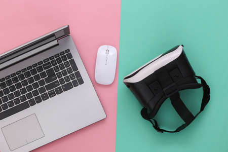 Laptop with VR glasses on blue-pink background. The virtual reality. Modern gadgets. top view. flat...