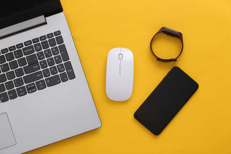 Modern gadgets. Laptop with pc mouse, smartphone, smart bracelet on a yellow background. top view. flat layの写真素材