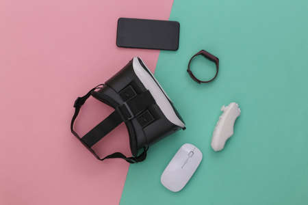 Modern gadgets and devices. Virtual reality headset with smartphone, controller, smart bracelet, pc mouse on blue-pink background. top view. Fly layの写真素材