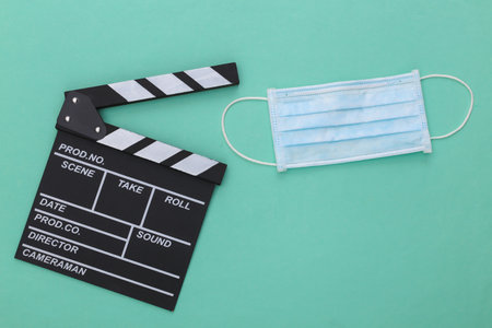 The downturn in the entertainment industry during covid-19. Movie clapper board with medical mask on a mint color background. filmmaking. top viewの写真素材
