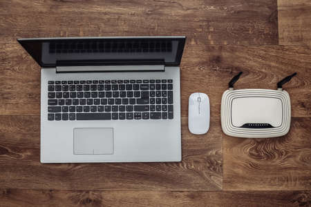 Laptop with pc mouse and wifi router on wooden floor. top view. Falt layの写真素材