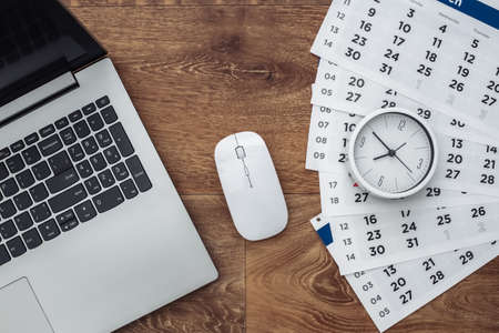 Laptop with sheets of the monthly calendar, clock on wooden background. top viewの写真素材
