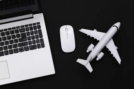 Travel flat lay. Laptop with pc mouse, plane on black background. top view