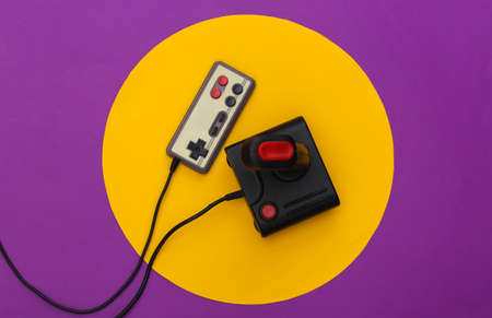 Retro joystick and gamepad on purple background with yellow circle. Conceptual studio shot....