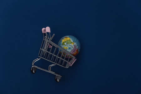 Shopping trolley with globe on classic blue background. global supermarket. Color 2020. Top view.の写真素材