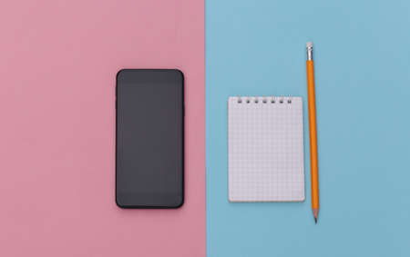 Notebook with pencil, smartphone on pink blue background. top view