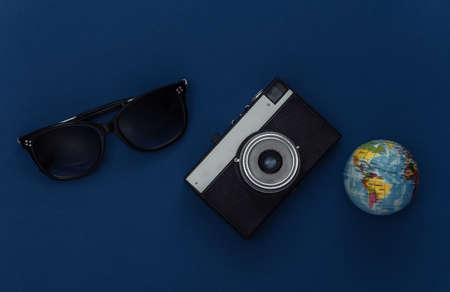 travel concept. Camera and globe, sunglasses on classic blue background. Color 2020. Top view.