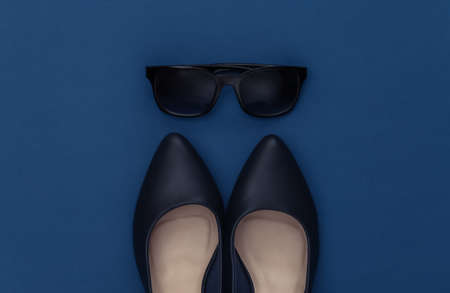 Fashionable leather high heel shoes and sunglasses on a classic blue background. Color 2020. Top...