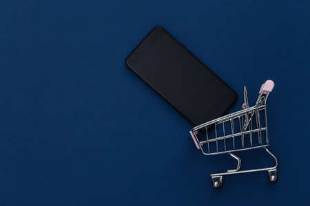 Shopping trolley with smartphone on classic blue background. online shopping. Color 2020. Top view.の写真素材