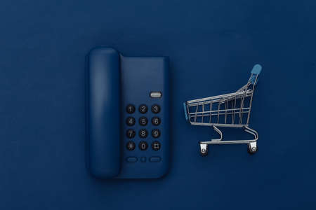 Landline phone with shopping trollety on classic blue background. Color 2020