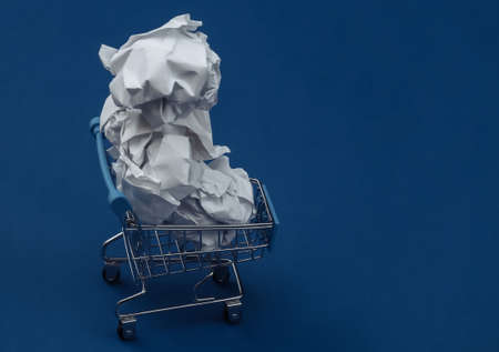 Shopping trolley with crumpled paper balls on classic blue background. Color 2020.