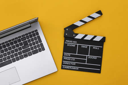 Movie clapper board with laptop on yellow background. Filmmaking, Movie production, Online cinema. top viewの写真素材