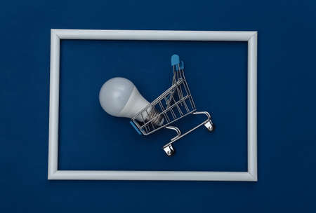 Shopping trolley and LED light bulb on classic blue background with white frame. Color 2020の写真素材