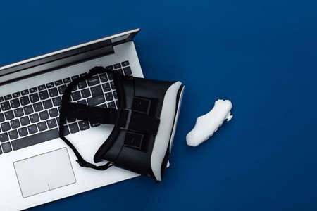Laptop with VR glasses, joystick on classic blue background. The virtual reality. Modern gadgets,...
