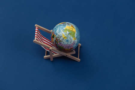 Beach deck chair with globe on classic blue background. Color 2020.