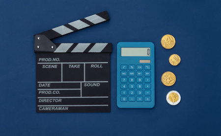 Movie clapper board and coins, calculator on classic blue background. Cinema fees. Filmmaking, Movie production. top viewの写真素材