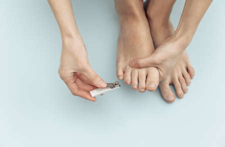 Woman cuts toenails with nail clippers on blue background. self care conceptの写真素材