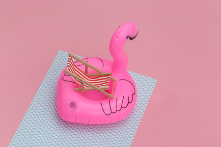 Inflatable pink flamingo with deck chair on pink blue pastel background. Summer vacation concept....