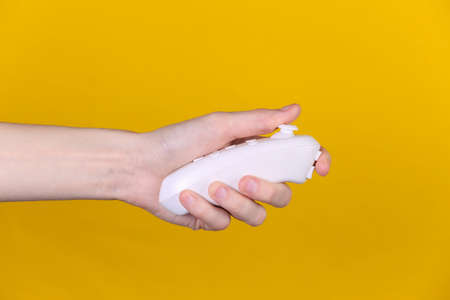 Hand holds modern joystick on yellow background.