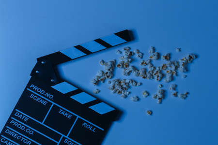 Film clapper board with popcorn in blue neon light. Cinema industry, entertainment. top view