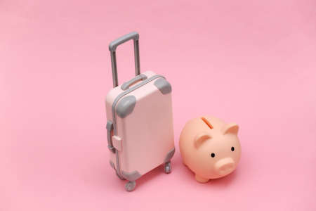 Travel or trip concept. Mini plastic travel suitcase and piggy bank on pink background. Minimal styleの写真素材