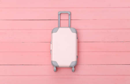 Flat lay vacation holiday and travel planning concept. Mini plastic travel suitcase on pink wooden...
