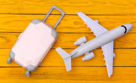 Flat lay vacation holiday and travel planning concept. Mini plastic travel suitcase, air plane on yellow wooden background. top viewの写真素材