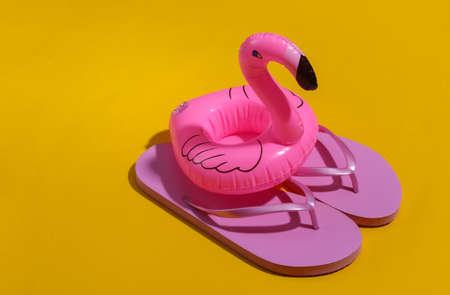 Inflatable pink flamingo with flip flops on yellow sunny background. Summer, beach vacation concept. minimalism.の写真素材