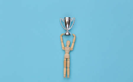 Happy wooden puppet holding a silver championship cup on a blue background