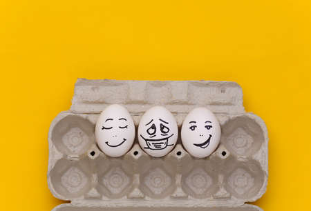 Covid-19 pandemic. Eggs tray with eggs by faces on yellow background. top viewの写真素材
