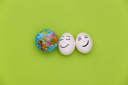 Happy couple chicken eggs faces and globe on green background. earth day
