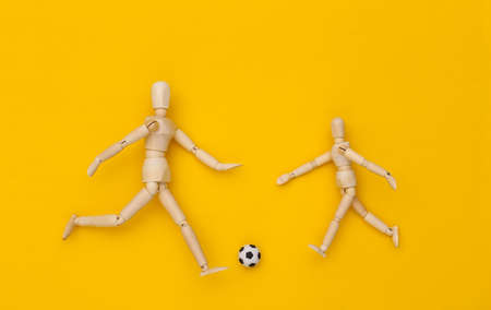 Two wooden puppet playing soccer with a ball on yellow backgroundの写真素材